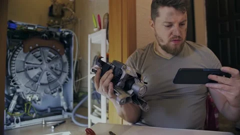 A man fixes a washing machine and watches instructions on his phone Stock Footage 155337750