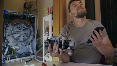 A man fixes a washing machine and watches instructions on his phone Stock Footage 155644224