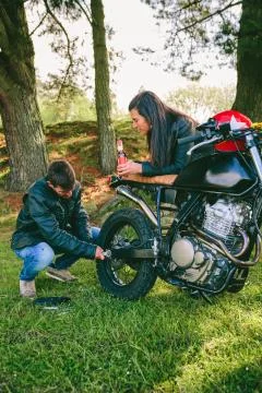 Man fixing his motorcycle while his girlfriend looks at him Stock Photos