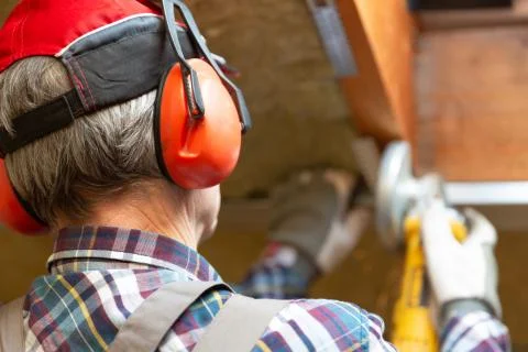 Man fixing metal frame using angle grinder on attic ceiling covered with rock Stock Photos
