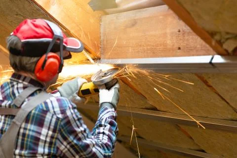 Man fixing metal frame using angle grinder on attic ceiling covered with rock Stock Photos