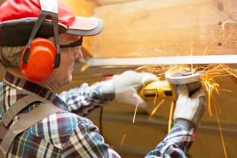 Man fixing metal frame using angle grinder on attic ceiling covered with rock Stock Photos