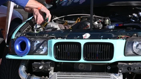 Man fixing something under the hood of a modified sport car with engine on Stock Footage 119951483