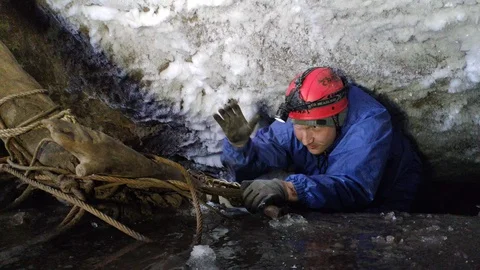 A man with a flashlight and a helmet in a cave crawls out of a crevice Stock Footage 129495128