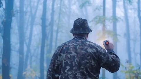 A man with a flashlight in his hand walks through the forest in the fog Stock Footage 118856718