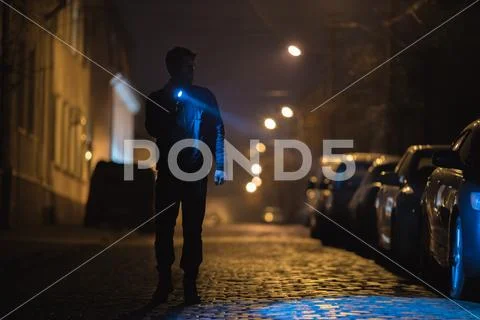 The man with a flashlight stand on wet road. Evening night time Stock Photos