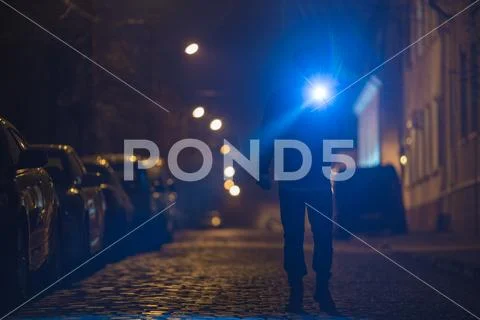 The man with a flashlight stand on wet road. Evening night time Stock Photos