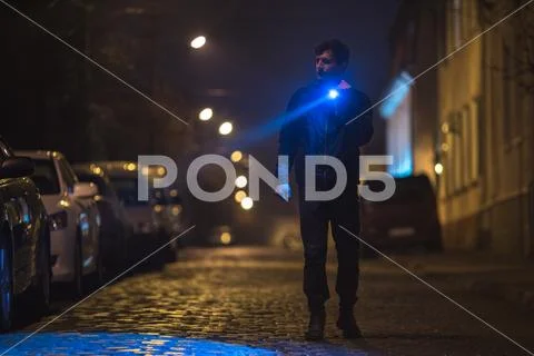 The man with a flashlight stand on wet road. Evening night time Stock Photos