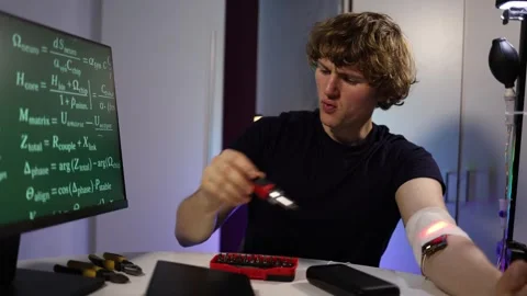 Man flexes arm while testing glowing implant and watching data in lab Stock Footage 324443520