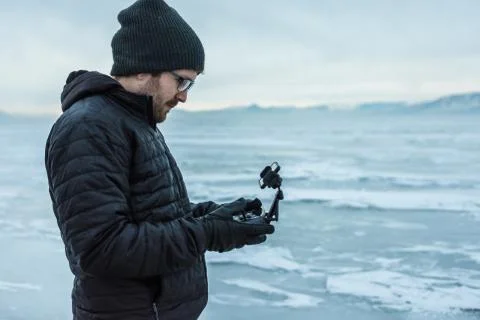 Man flies black drone helicopter over frozen lake Stock Photos