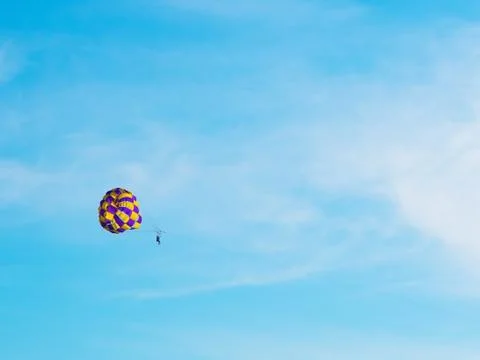 A man flies in the sky on a bright white-yellow parachute against a clear blue Stock Photos