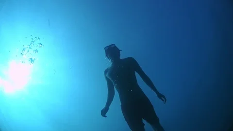 A man in flippers floats to the surface of the sea in the sun's rays. Stock Footage 124875462