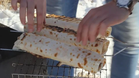 Man flips grilled roll of pita with some filled on bbq lattice, winter camping Video stock 165608089