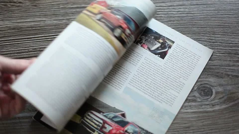 A man flips through the American magazine Car and Driver lying on the table. Stock Footage 237449384
