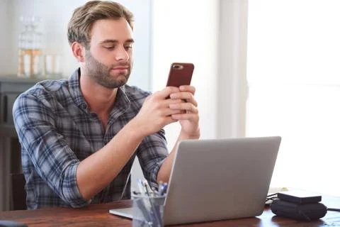 Man flirting on his phone while sitting at his desk Stock Photos