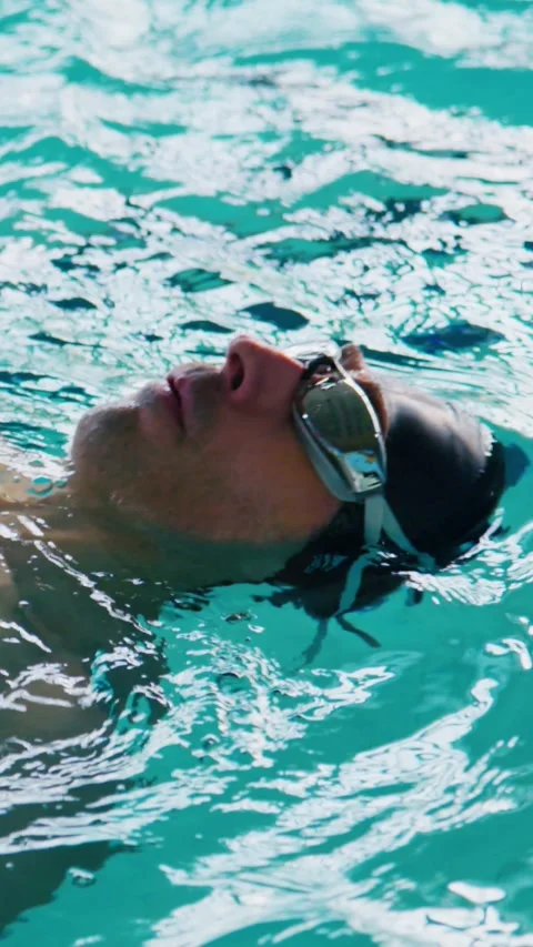 Man floats effortlessly on back in bright pool, eyes closed Stock Footage 346457990