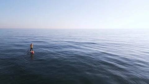 Man floats on SUP board on the clear azure calm waters of the Black Sea, aerial Stock Footage 229423652