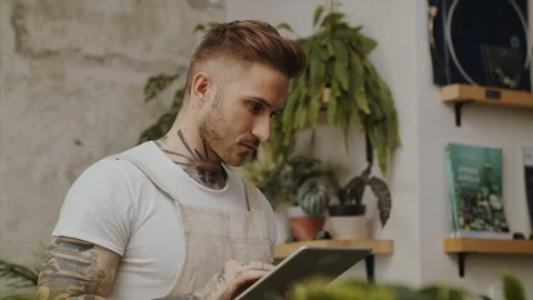 Man florist standing in flower and plant shop, using tablet. Vídeos de archivo 123776017