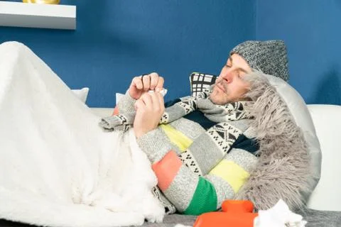 Man with flu on the couch is taking medication Stock Photos
