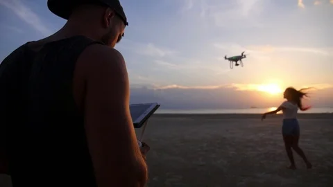 Man with Flying Drone with Remote Control At Sunset Beach Stockbeeldmateriaal 74267142
