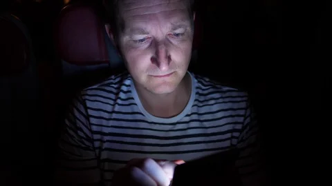 Man is flying by the plane at night. he reads something in his phone in the dark Stock Footage 97190378