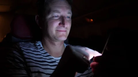 Man is flying by the plane at night. he reads something in his phone in the dark Stock Footage 97191606