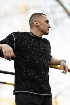 Man is focused and relaxed while leaning against exercise equipment in park. sun Stock Photos