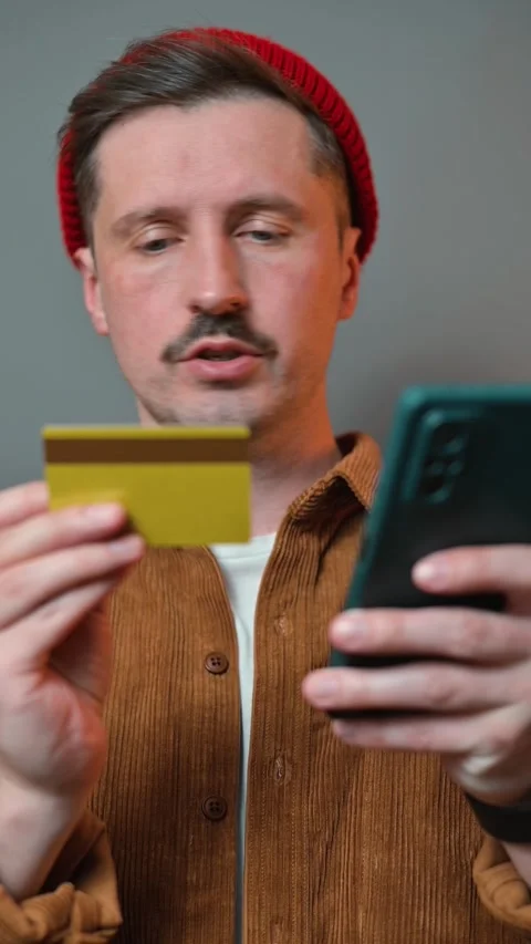 A man is focused on his smartphone while operating a credit card. He appears 動画素材 337643114