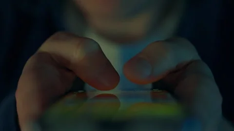 A man focused on a mobile phone screen explores social media in a dark room, Stock Footage 255682728