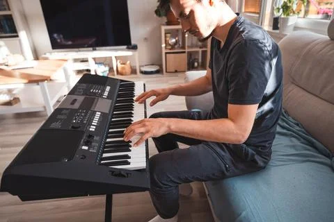 Man focused on playing a digital keyboard in a sunlit living room, surrounded Foto stock