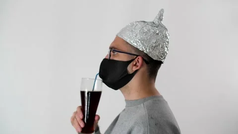 Man in a foil hat and a protective mask drinks beer through a tube from a glass. Vídeos de archivo 131711473