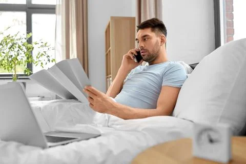 Man with folder calling on phone in bed at home Stock Photos