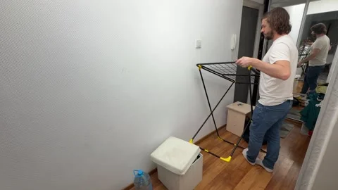 Man folding a clothes drying rack in a narrow hallway at home, preparing space Stock Footage 336981434