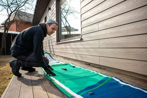 Man folding an inflatable stand-up paddleboard (SUP) on a wooden deck next .. Stock Photos
