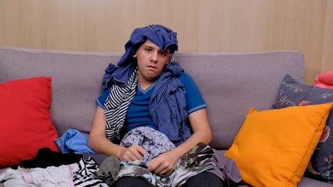 Man folding laundry at home. The man is covered in clothes. Tired man Stock Footage 124873376