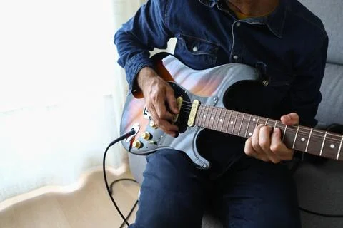 A man in the foreground practicing his electric guitar lessons at home Stock Photos