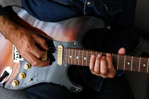 A man in the foreground practicing his electric guitar lessons at home Stock Photos