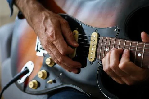 A man in the foreground practicing his electric guitar lessons at home Stock Photos