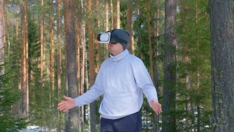 Man in forest among pine trees in vr googles waving hands and turning sides. Stock Footage 129600569