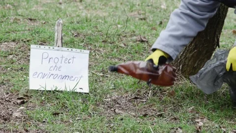 A man in the forest bends down and puts an old plastic bottle in a plastic g Stock Footage 236190689