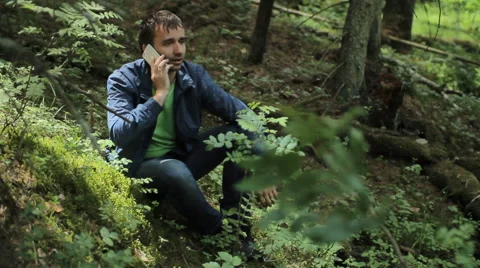 The man in the forest call by smartphone. It sits on a small cliff green Stock Footage 64531733
