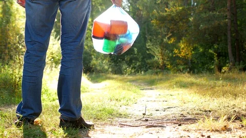 A man in a forest clearing stands with a package of garbage in his hands, a Stock Footage 96077157