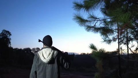 Man in a forest holding a gun looking at the horizon at dawn. Stock Footage 76443731
