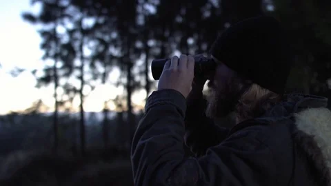 Man in a forest looking to the horizon with binoculars at dawn. Stock Footage 76443990
