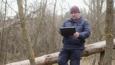 A man in the forest looking through photos on his tablet while sitting on a Vídeos de archivo 170983235