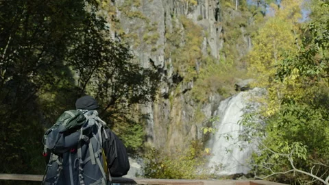 A man in the forest looks at a waterfall with a backpack Stock Footage 201402652