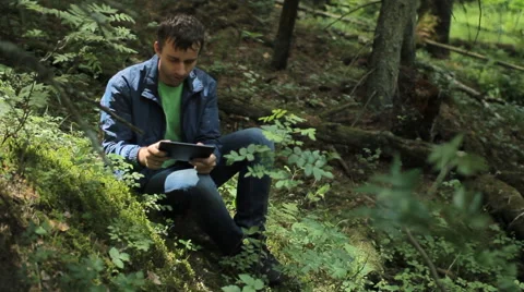 The man in the forest play on tablet in game. It sits on a small cliff green Stock Footage 64531416