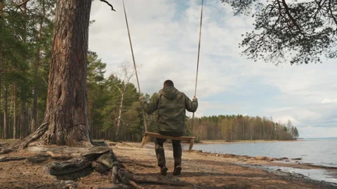 A man in the forest swinging on a swing. Rope swing on a forest lake. Видео 197284444