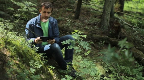 The man in the forest touch tablet. It sits on a small cliff green Stock Footage 64525766