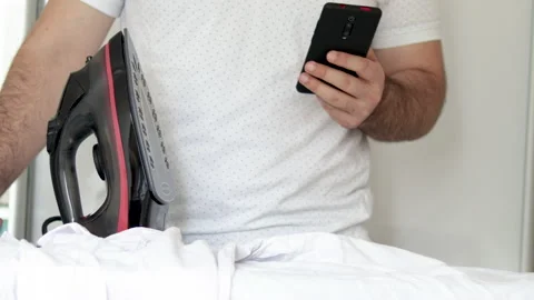 Man forgets to stand up iron from white shirt and is playing,using mobile phone Vidéo 197641491